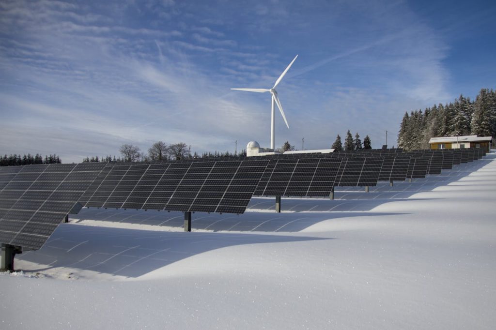 solar-panels-on-snow-with-windmill-under-clear-day-sky-433308 Solar panels and wind turbine in a snowy landscape, showcasing renewable energy sources.